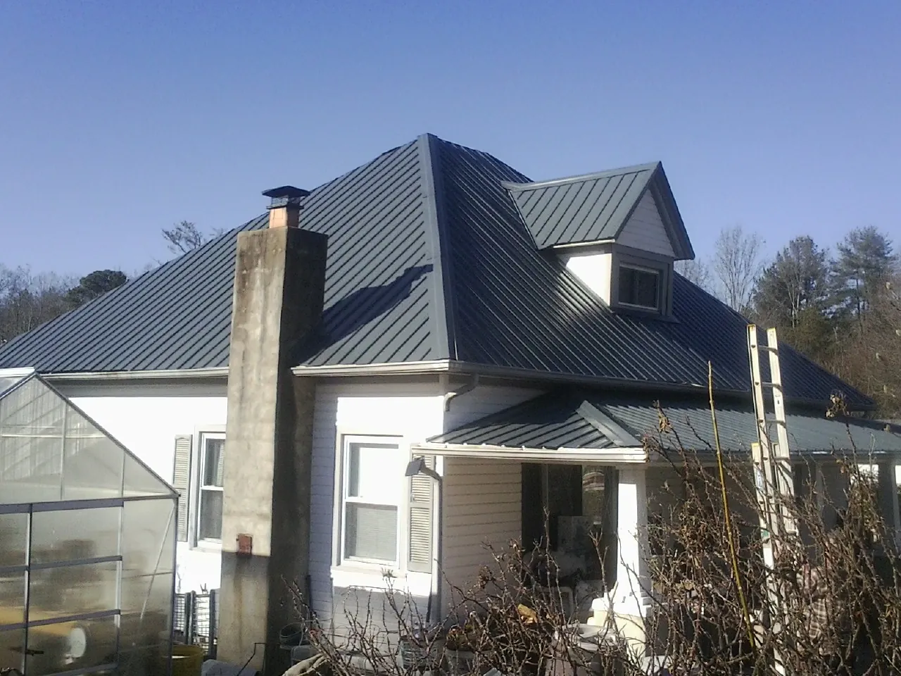 Dark blue standing seam metal roof on a white farmhouse with dormer — Slate & Tile Roof Repair by Roofing Brothers in North Liberty