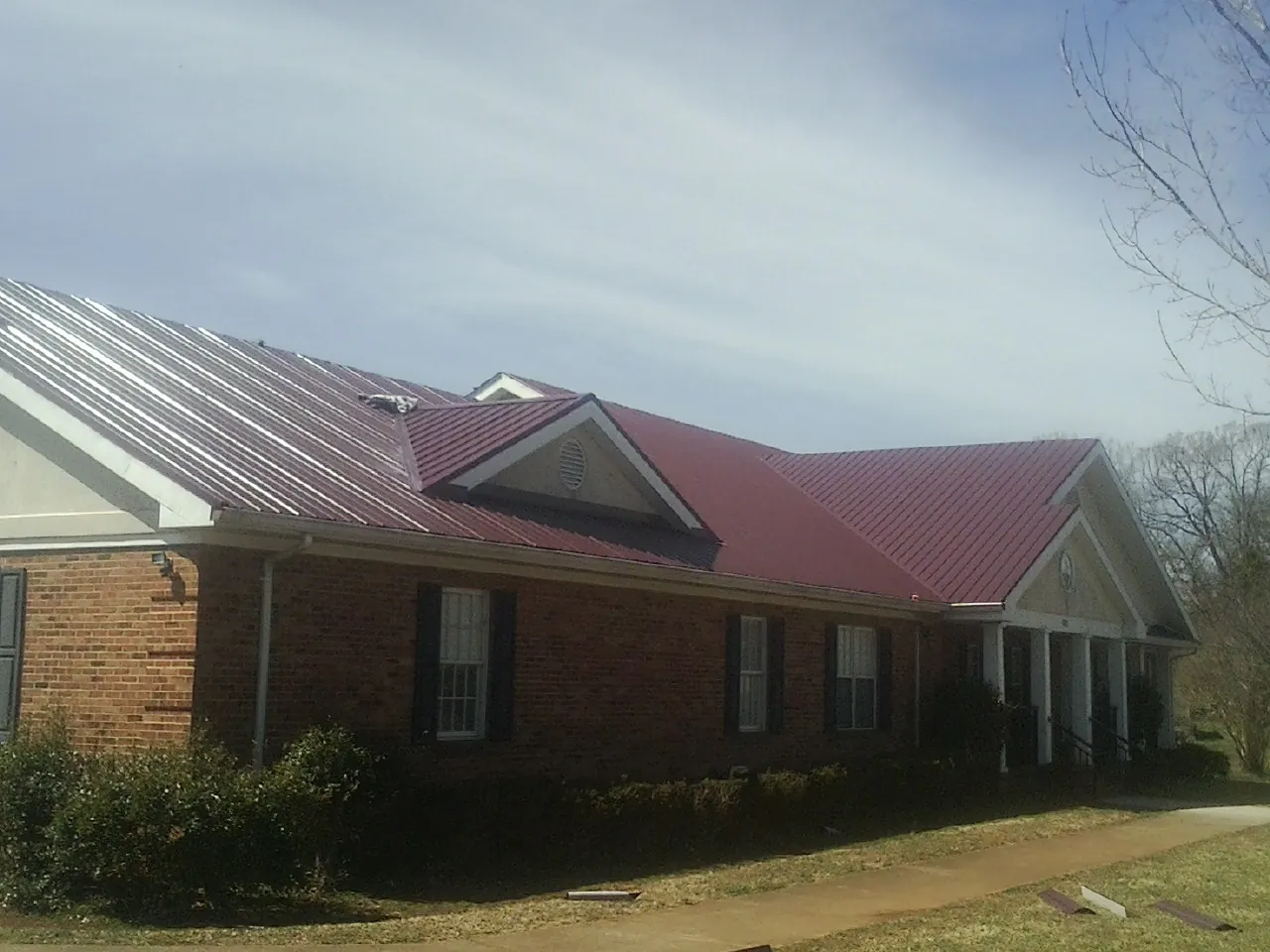 Red metal roof with gabled entries on a long brick building, from a Hail Damage Roof Repair job in North Liberty