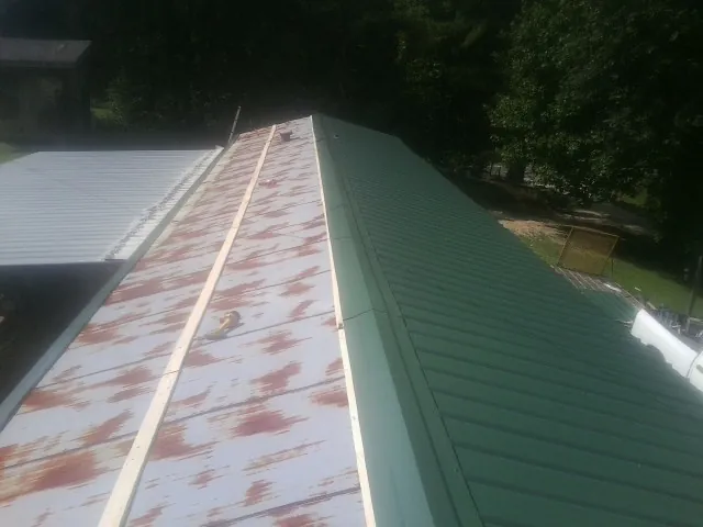 Old rusted panels beside newly installed green metal roofing — Wind Damage Roof Repair by Roofing Brothers in North Liberty