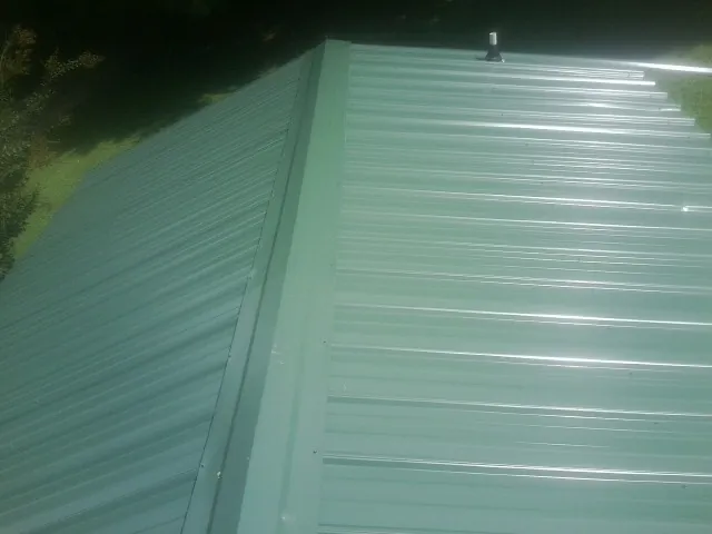 New green metal panels meeting at the ridge of a roof — Flat Roof Repair work by our crew in North Liberty